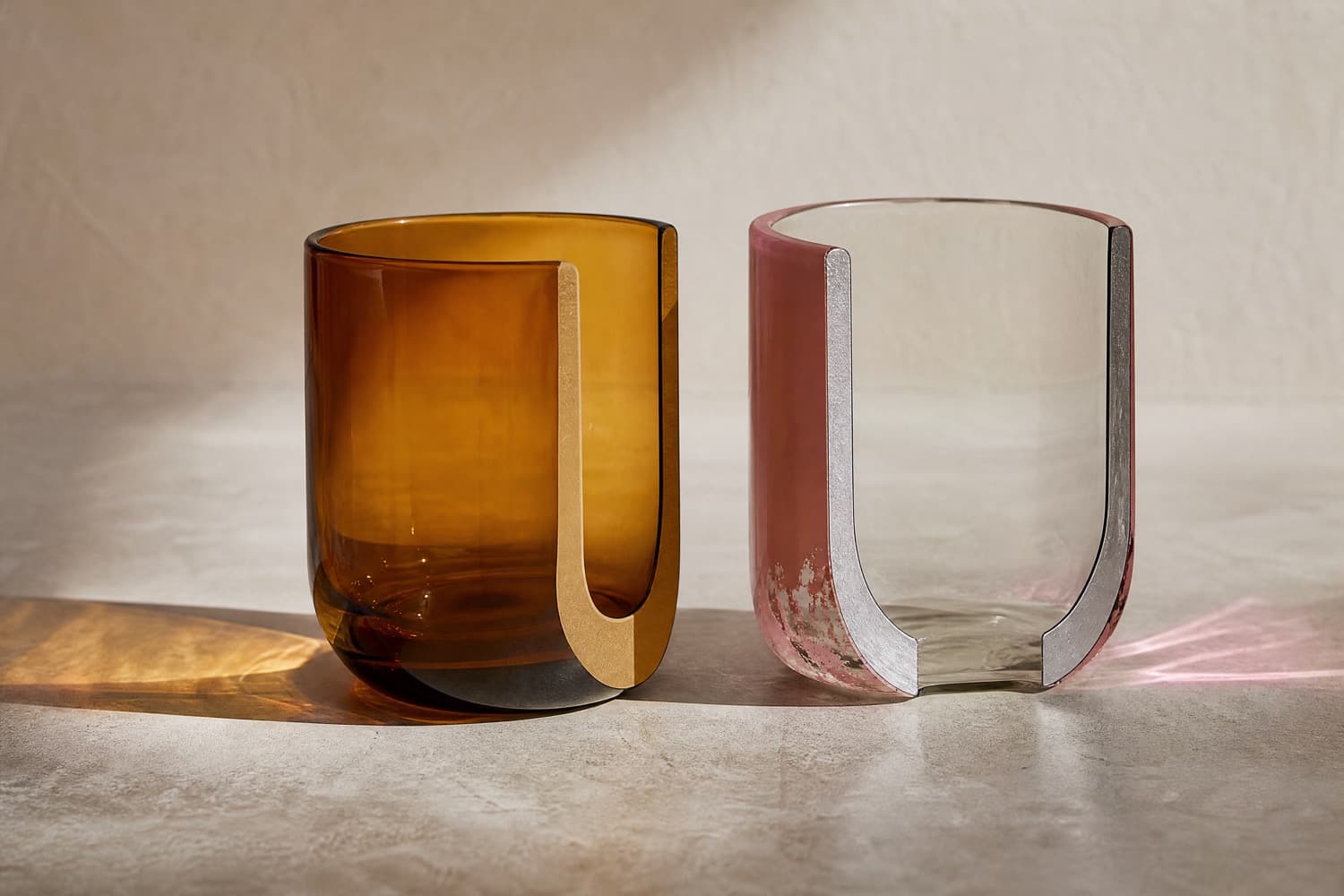 Two glass tumblers shown in cross-section: the left one is amber through the full thickness of its wall, the right one is clear glass with a thin pink surface layer that is visibly worn near the base.