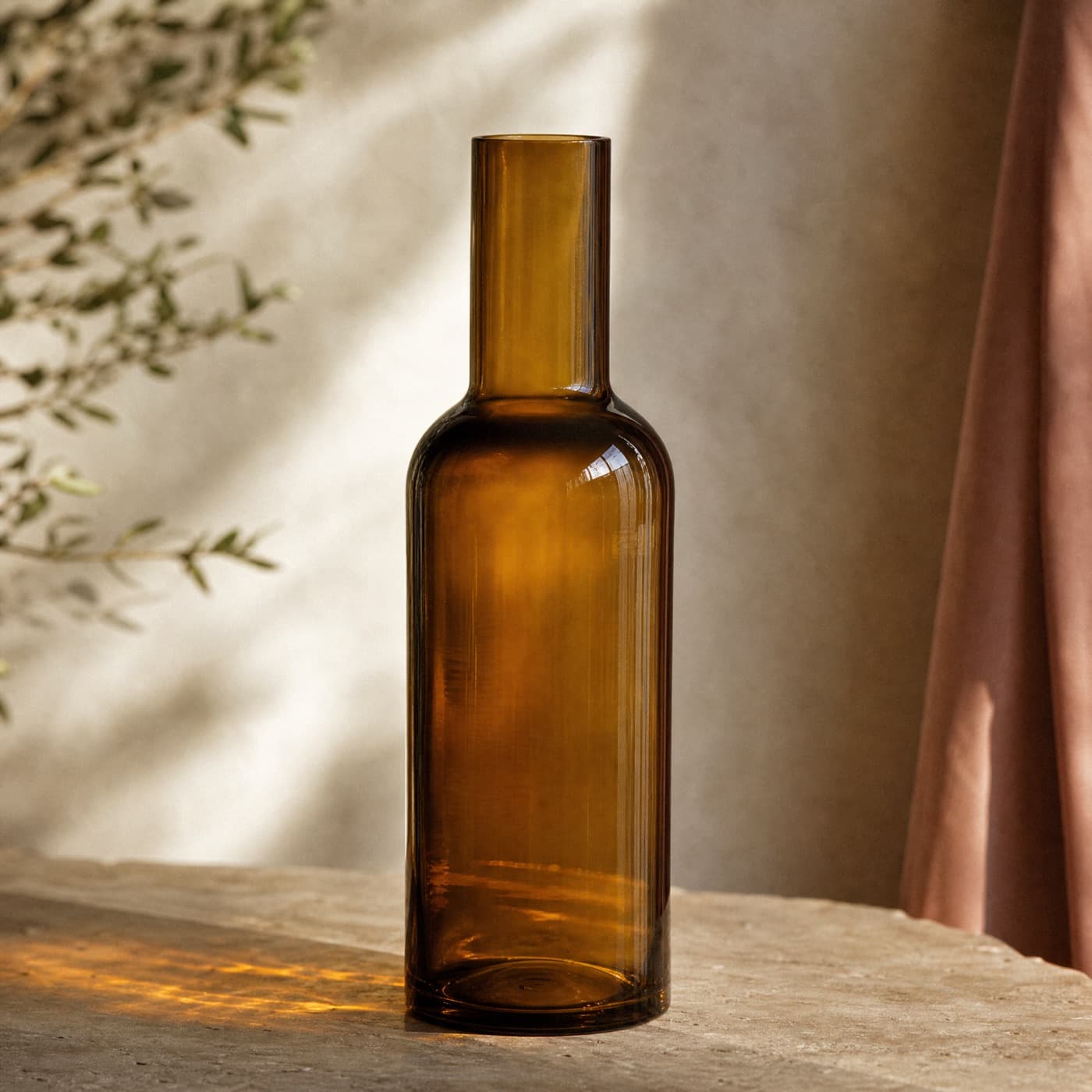 Tall amber bottle vase with a pronounced shoulder, backlit so the shoulder reads darker than the neck.