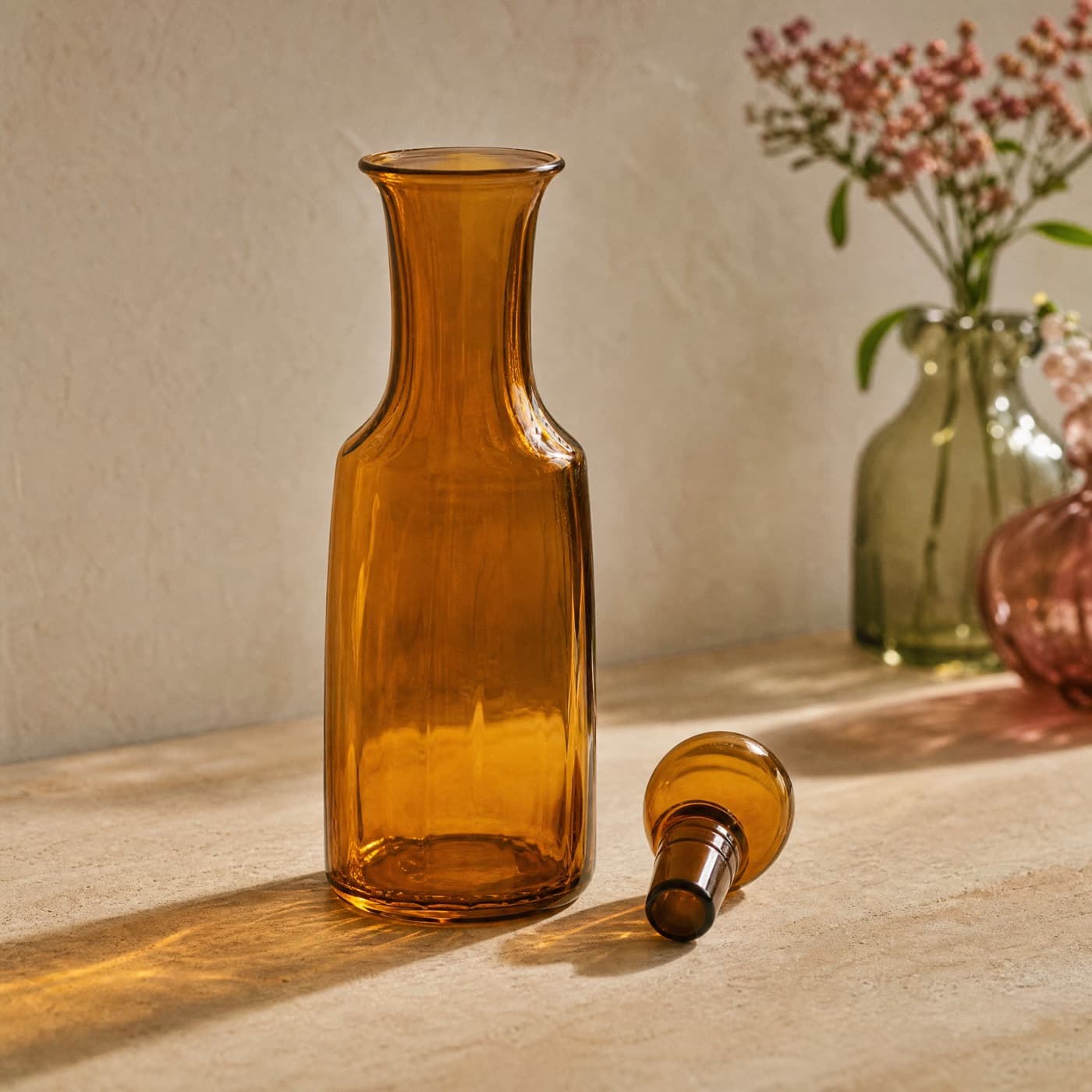 Amber carafe with a ground glass lid resting beside it, lit from a window behind.