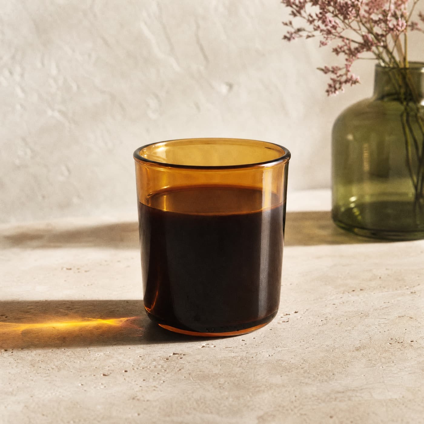 Amber borosilicate coffee glass with coffee inside, backlit, casting a deep amber patch on the counter.