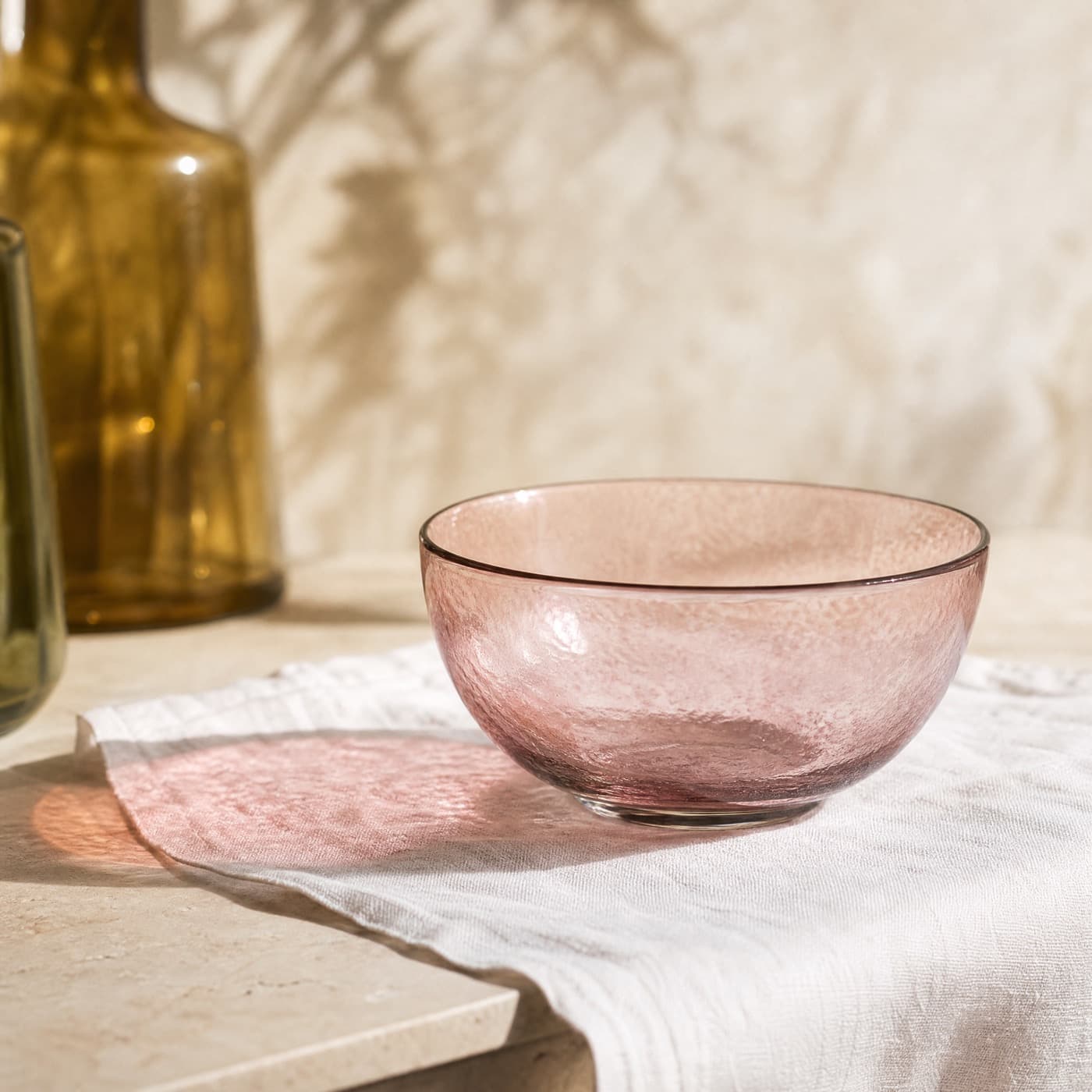 Shallow misty rose glass dessert bowl on a white cloth, a pink oval of light directly beneath it.