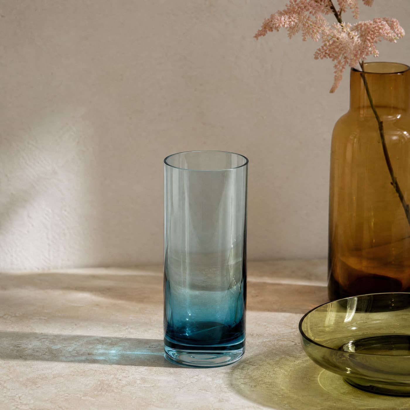 Tall sea-blue highball glass backlit, colour deepening toward the heavier base.