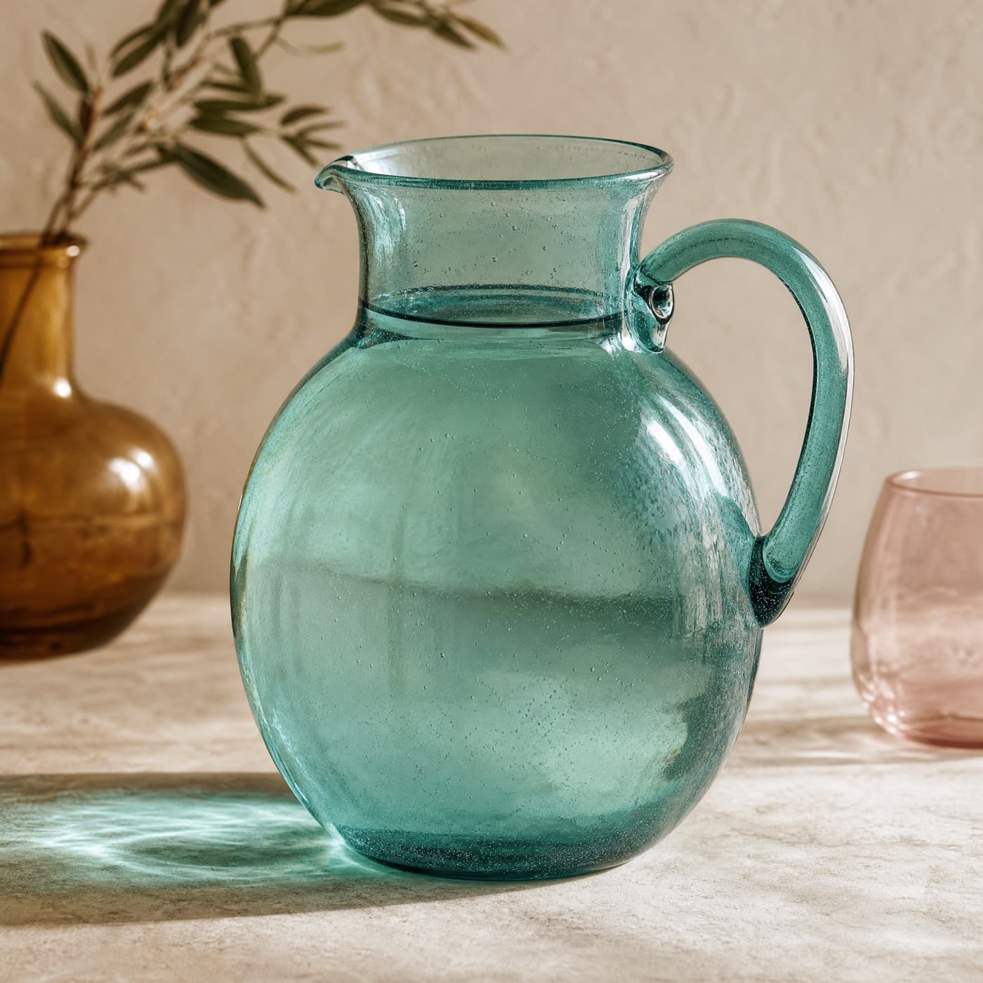 Sea-blue glass juice jug with a handle, filled and backlit against a bright window.