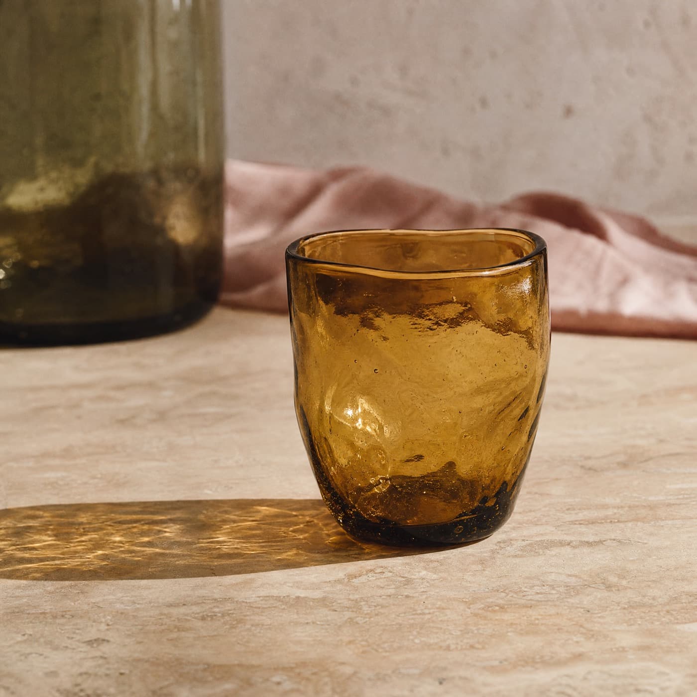 Mouth-blown amber glass with visible bubbles and an uneven wall, strongly backlit on a pale table.