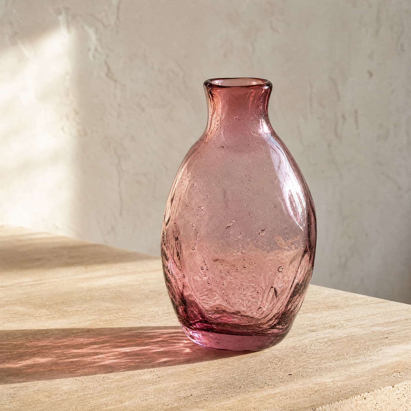 Mouth-blown misty rose vase with visible bubbles and an uneven wall, casting a mottled pink light.