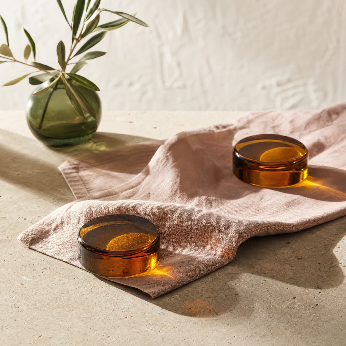 Two solid amber glass discs holding down a linen napkin on an outdoor table in bright sun.