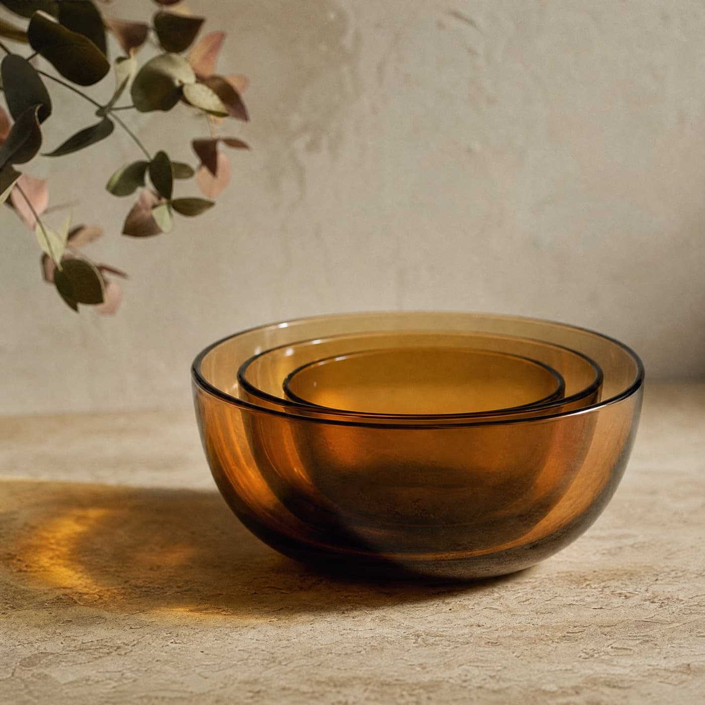 Three amber glass bowls of increasing size nested together, backlit so the overlapping walls read darker.