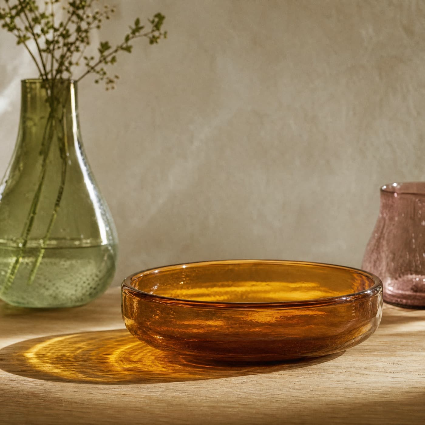 Wide amber glass serving bowl on an oak table, casting a large warm patch of light onto the wood.