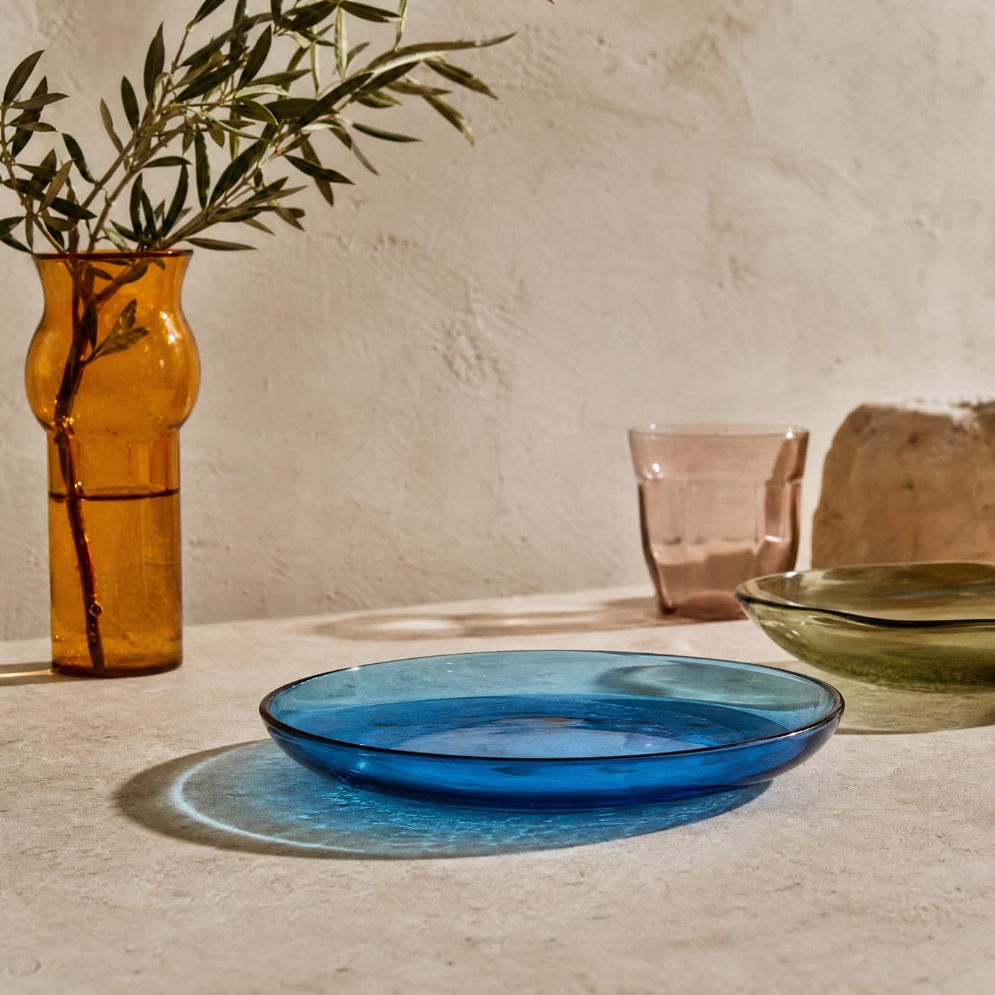 Sea-blue glass side plate in direct sun, casting a sharp blue disc of light onto the table.