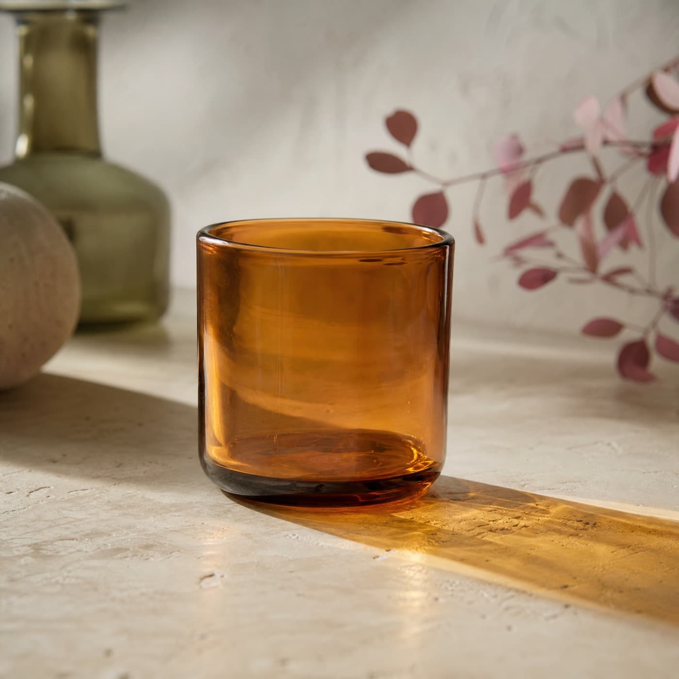 Amber water glass photographed against the light, casting an amber patch on a pale oak surface.