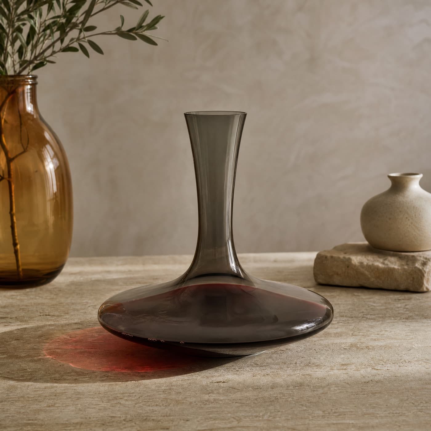 Smoke-grey wine decanter with a wide base, holding red wine, lit from behind on a dark table.